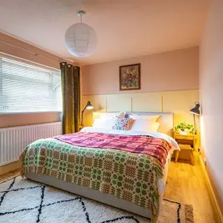 Bedroom with double bed and colourful blankets, bedside tables and lamps, green curtains