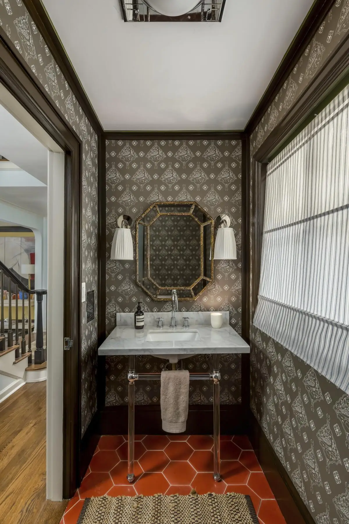 A powder room that features Katie Ridder's Oiseau wallpaper, hex barn-hued tile,  contemporary lighting and a marble sink. 