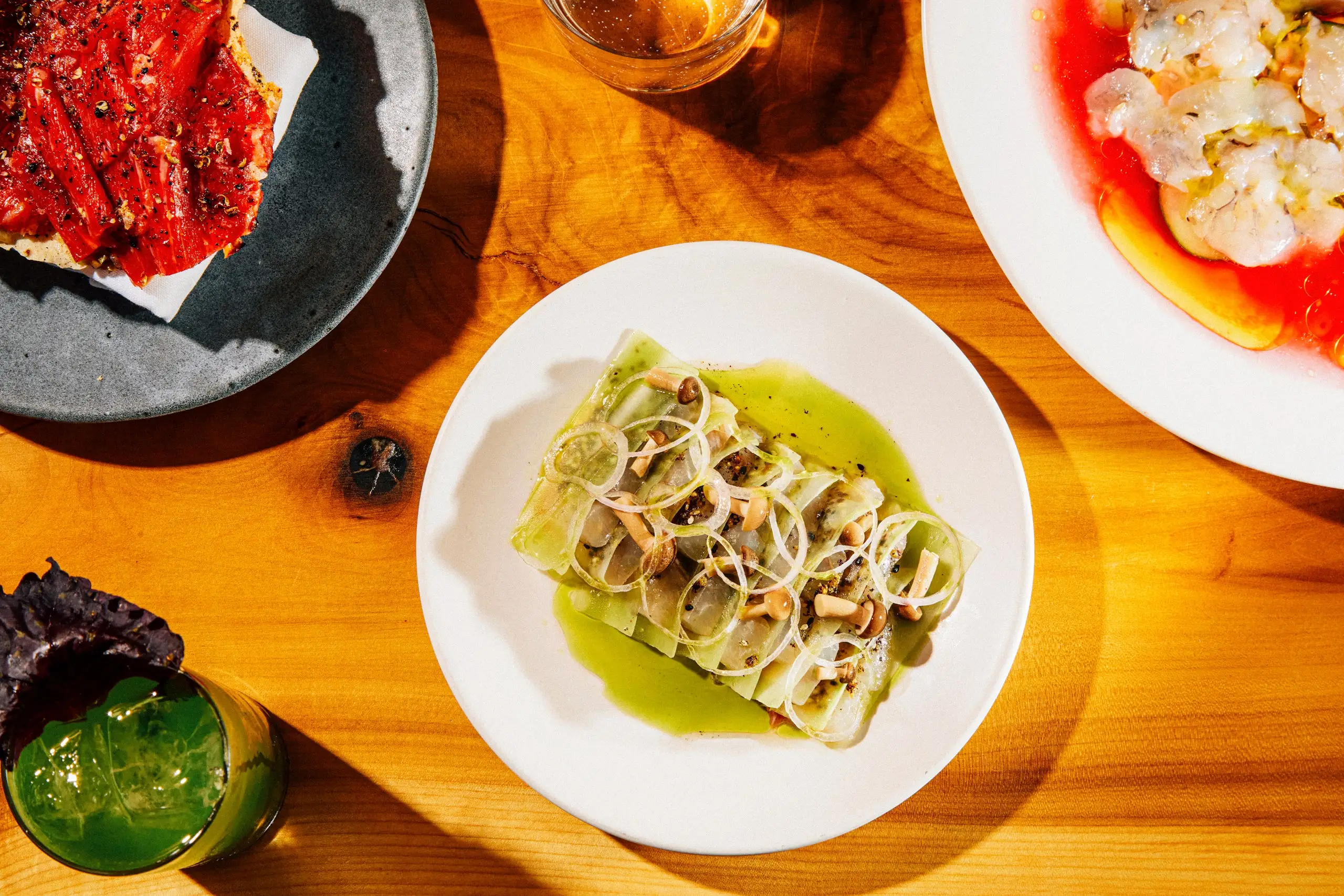 A plat of crudo on a wooden table alongside other dishes