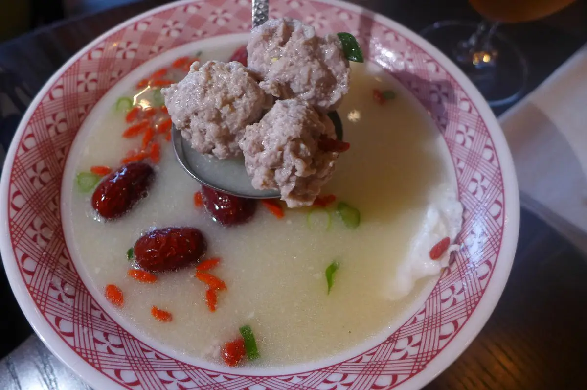 A milky broth with big red dates and three meatballs in a spoon held up.