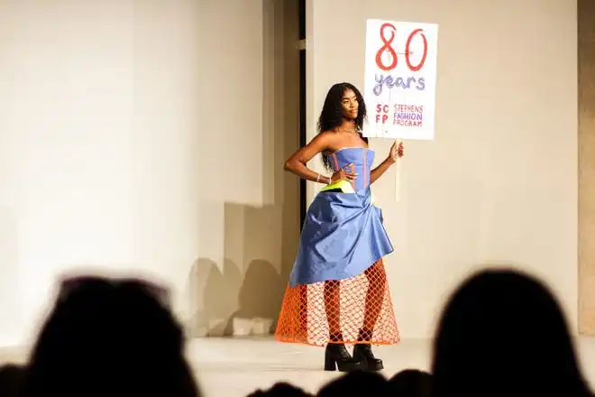 Chante Stonewall holds up a sign commemorating Stephens College's 80th annual fashion show while modeling a blue corset with a skirt designed by Ava Hercules Saturday, April 13 at Windsor Auditorium Stephens College in Columbia.