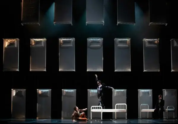 Photo of dancers performing in front of a backdrop of twin beds