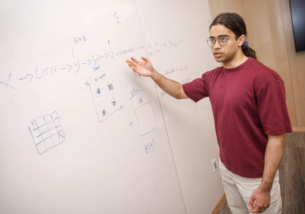 Mozes Jacob pointing to an equation on a white board.