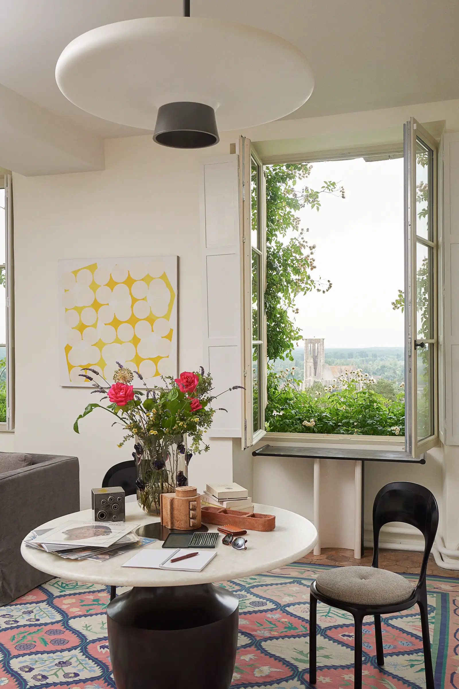 living room with white pendant light above white table with flower vase notebooks other vessels two black chairs with...