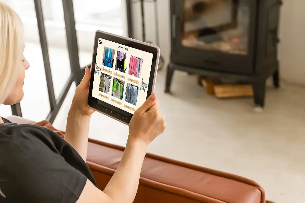 Back view of woman doing shopping online on website with digital tablet at home