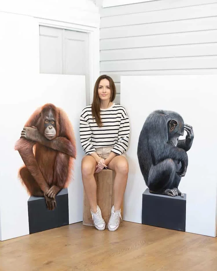 UK-based artist Sophie Green is photographed amongst two of her most recent paintings that are part of the Commodities collection. Her goal is to bring light to the ways that humans use nature to their own benefit, instead of showing it the respect it deserves.