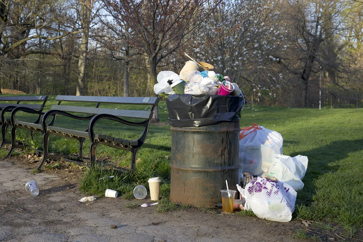 An overflowing trash can in a city park.