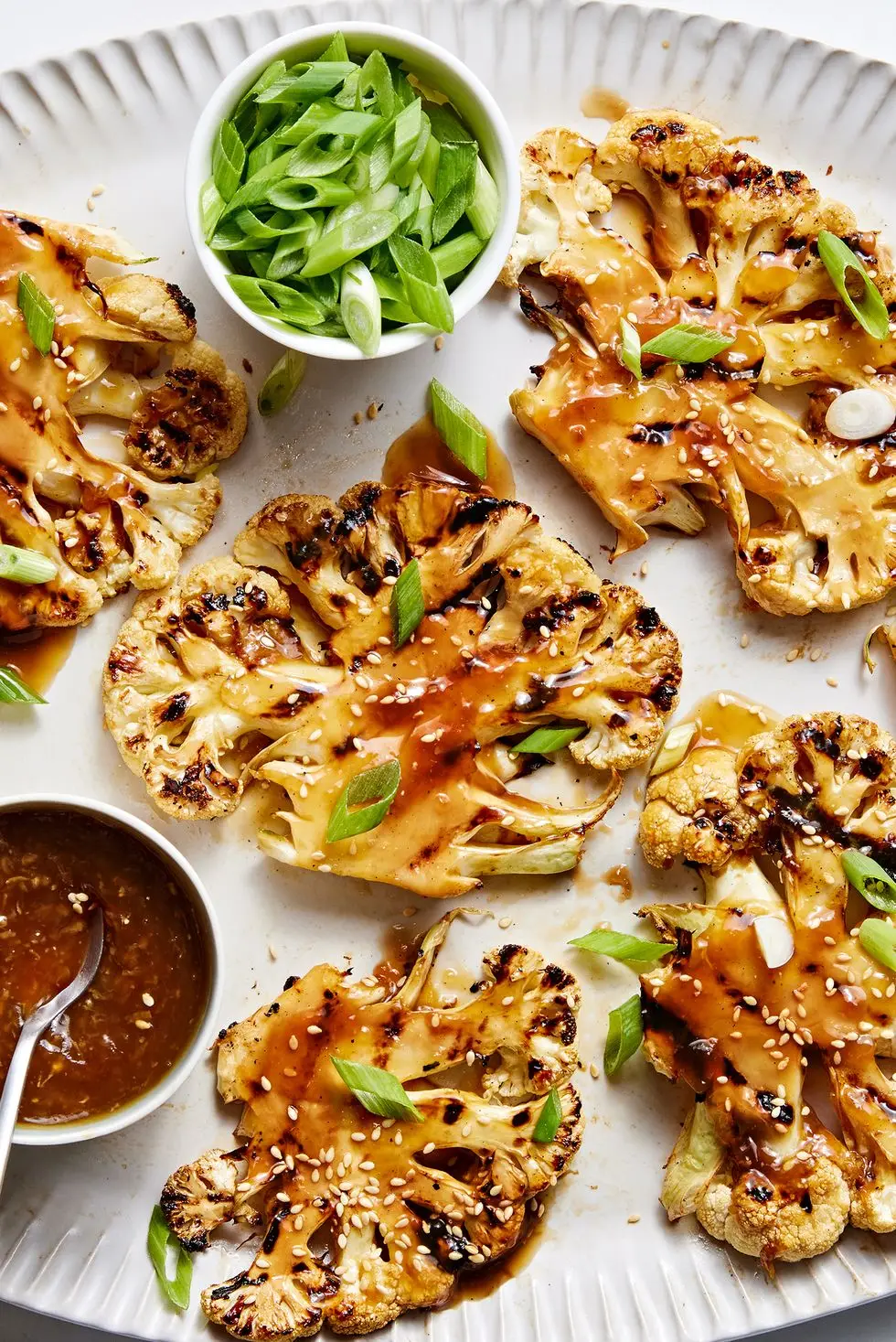 grilled teriyaki cauliflower steaks on a platter with more teriyaki sauce and scallions