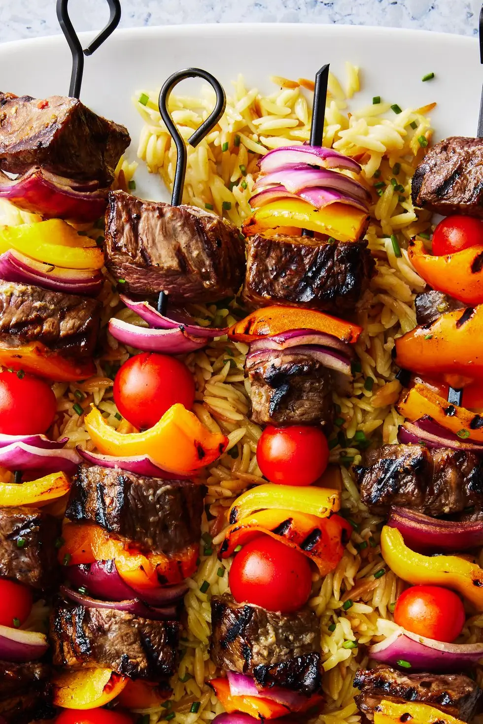 steak kebabs with peppers on top of orzo with a spinach cucumber salad