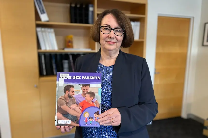 Aa woman stands holding a book titled same-sex parents