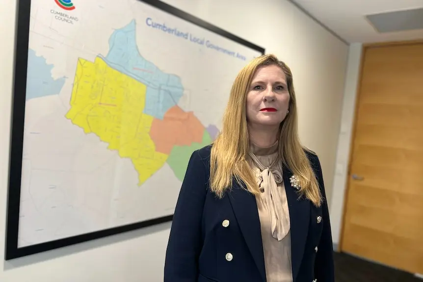 A woman with long blonde hair stands in front of a framed map