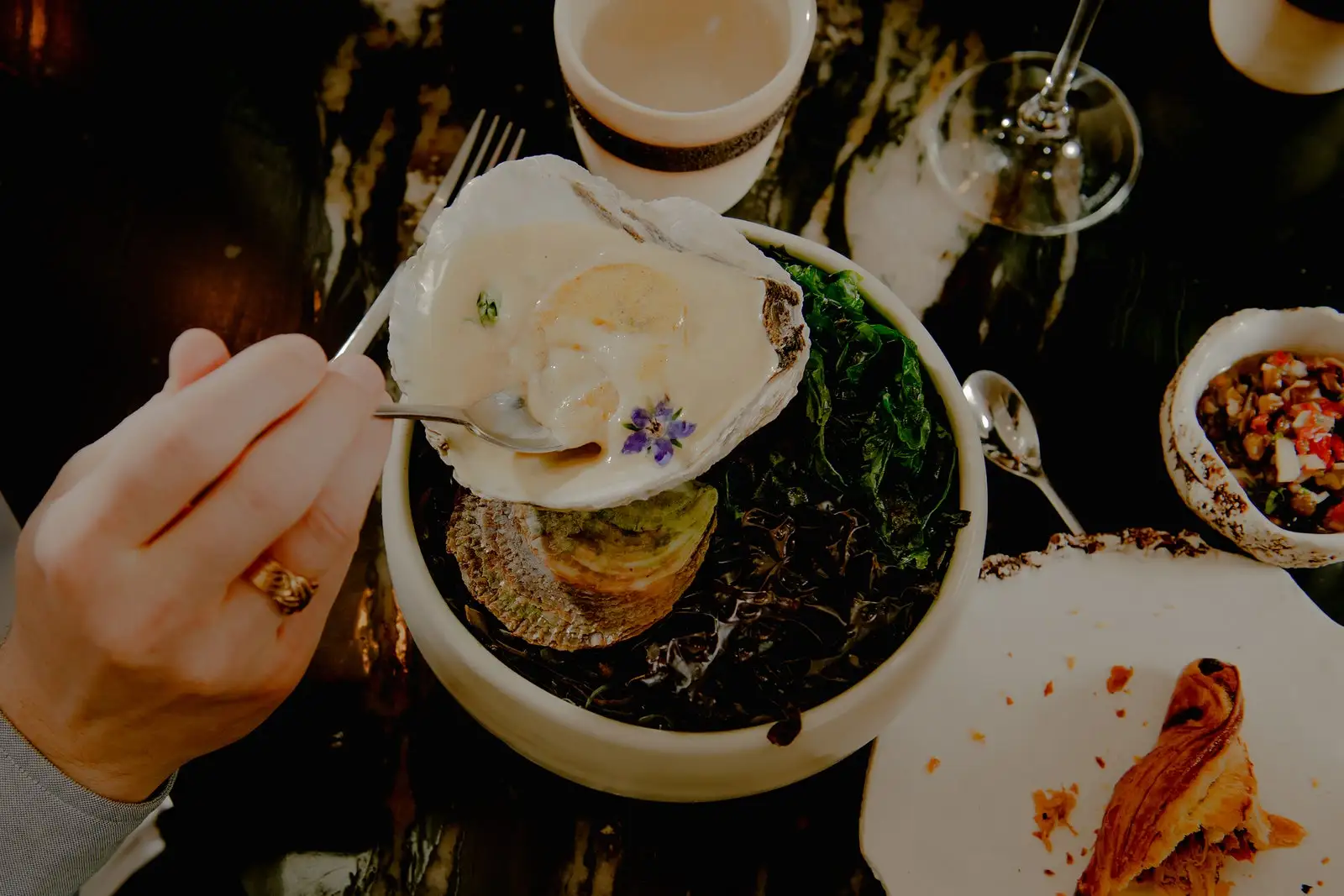 A diners hand scooping up an oyster in sauce.