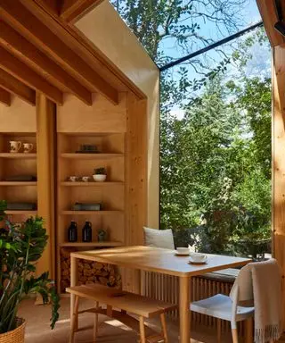 A wooden lake house with a full-wall window, a dining table and built-in shelving on the walls