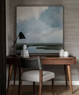 A wooden desk with a large landscape painting and a gray chair in front