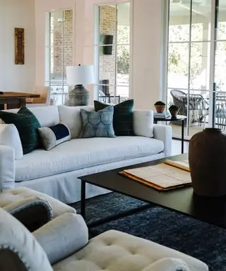 A lake house living room with a white sofa, blue area rug and floor to ceiling windows with a view