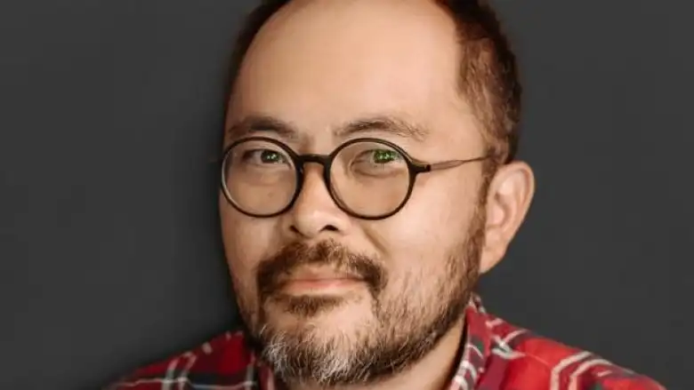 A bearded Asian man with round dark-rimmed glasses wearing a plaid shirt