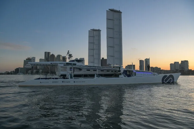 A boat with large vertical sails approaches Boston's shoreline.