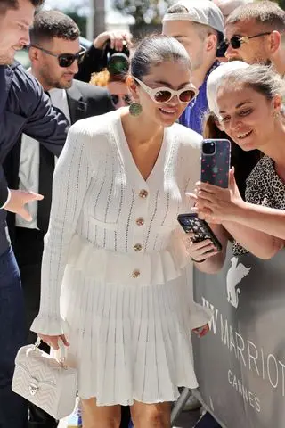 Selena Gomez poses with a fan at the Cannes film festival in a white self portrait dress