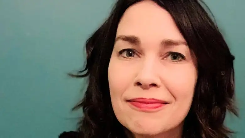 A woman with long black hair against a teal backdrop.