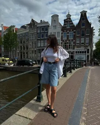 Woman on street wears long denim shorts, white shirt and sandals