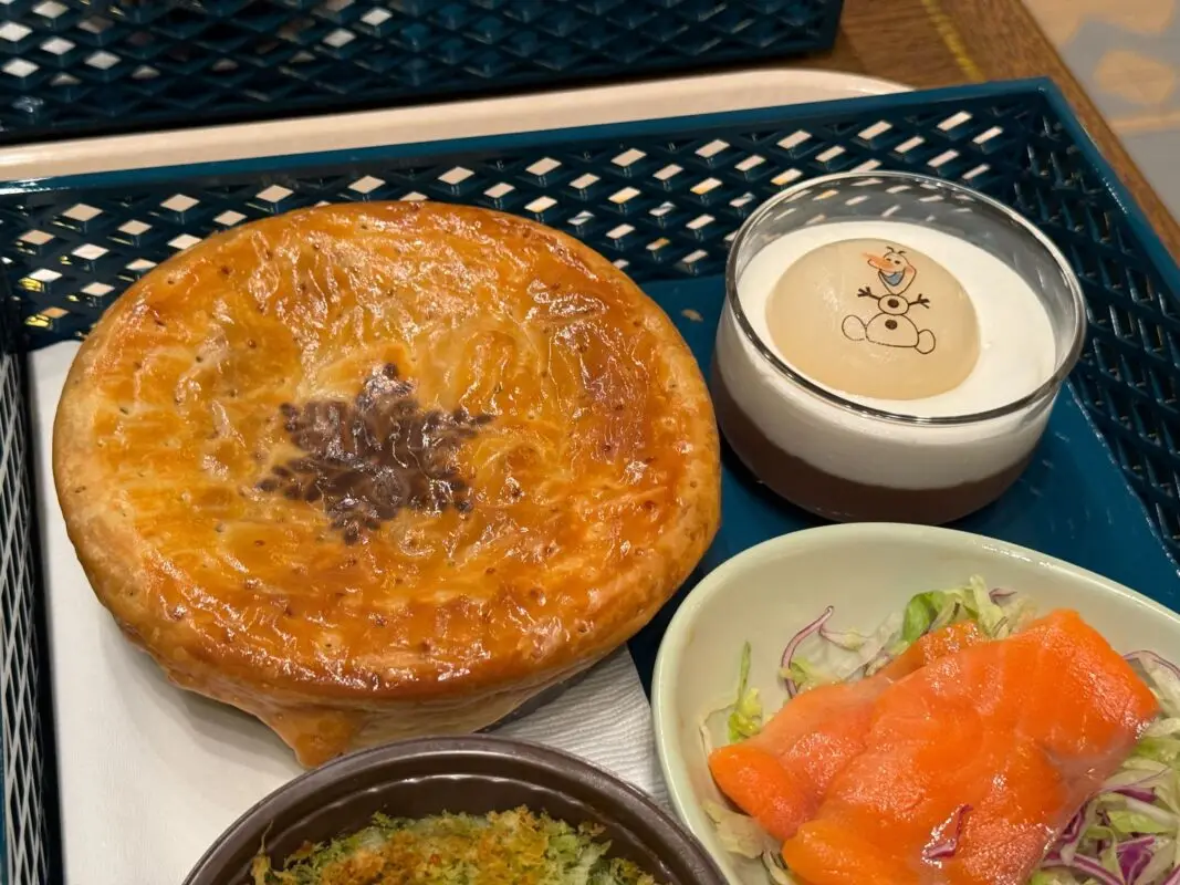 A baked pie, dessert with a character decoration, salad with smoked salmon, and a dish with vegetables are served on a dark blue tray.