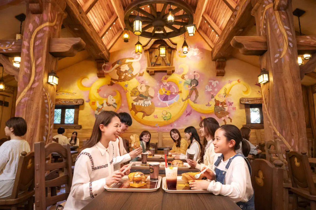 Guests enjoy meals at a wooden table in a themed restaurant with fairy tale murals on the wall.