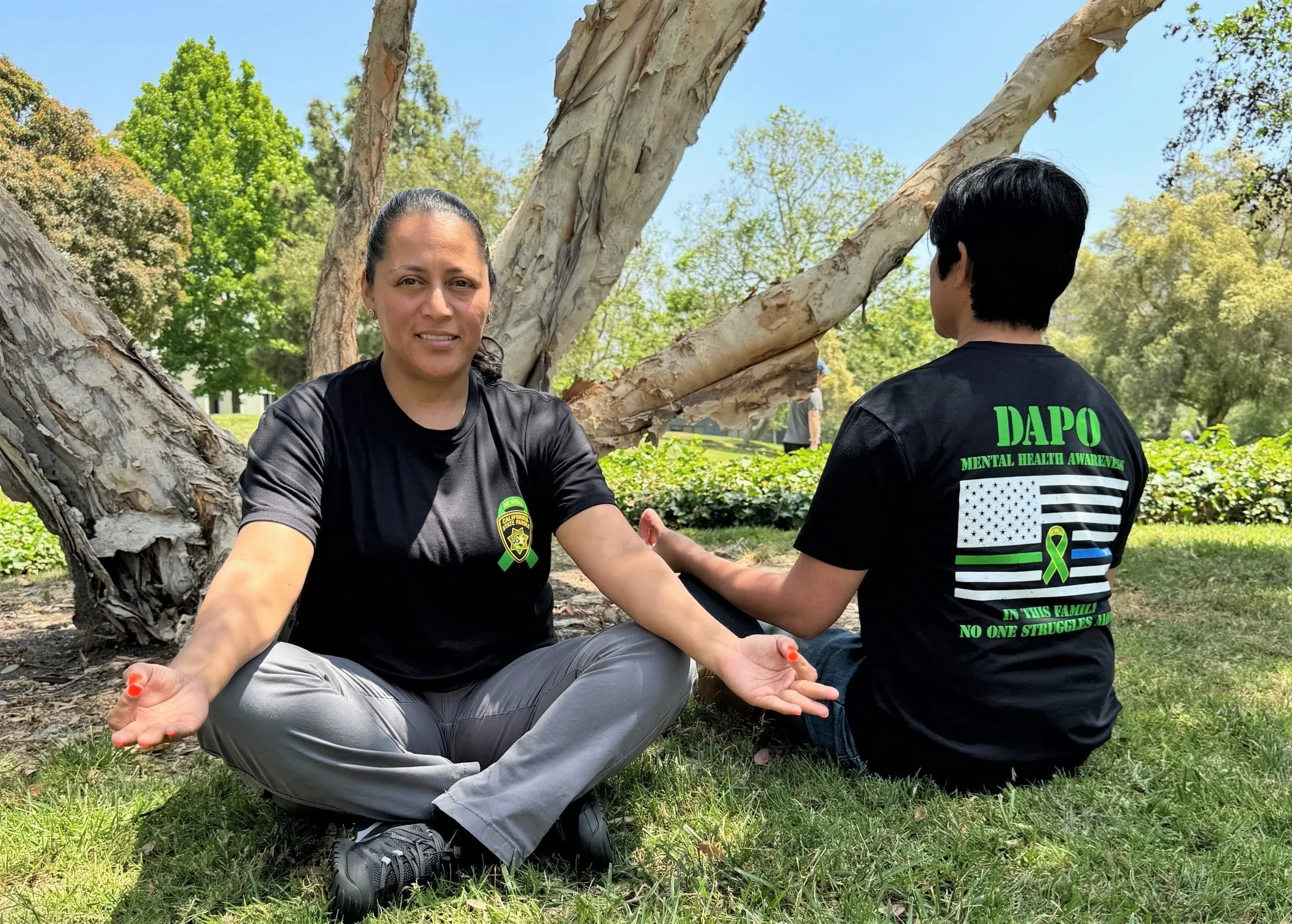 DAPO mental health t-shirt being worn by two people meditating on a lawn.