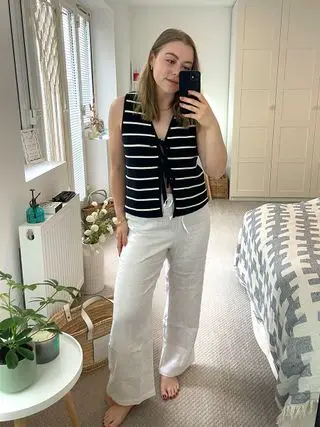 Woman wears striped knit waistcoat, linen white trousers