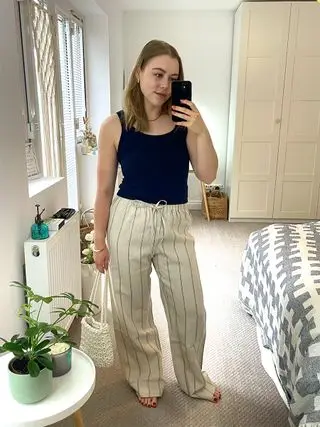 Woman in mirror wearing tank top, striped linen trousers