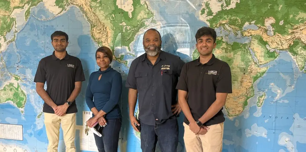 Two male college students and a female and male high school teacher stand in front of a map on a wall.