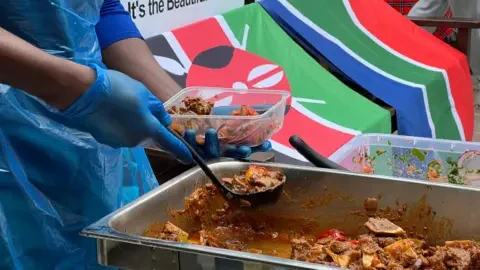 A close up of someone wearing plastic gloves scope a curried meat into a plastic Tupperware container