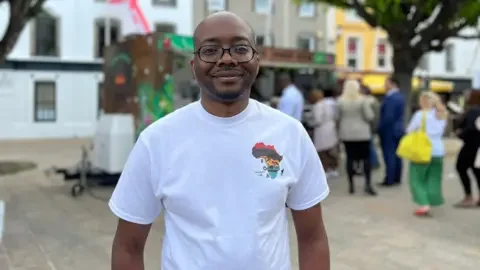 Washington smiles at the camera as people queue for food behind him