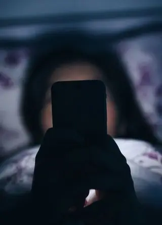 Woman texting and reading on smartphone in bed in midnight.