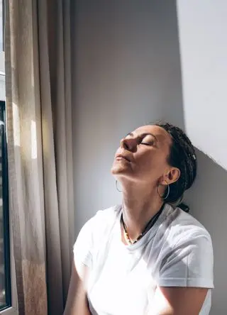 Portrait of a woman sitting by the open window at the white wall.