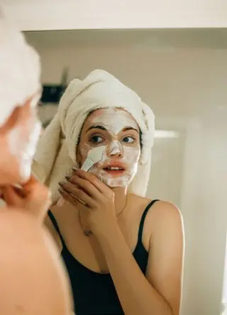 Side view shot of young woman applying facial cosmetic mask in bathroom.