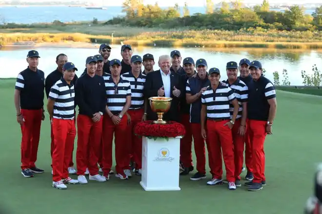In 2017, President Donald J. Trump poses with the U.S. team and the Presidents Cup trophy after the final round singles matches of The Presidents Cup golf tournament at Liberty National Golf Course.