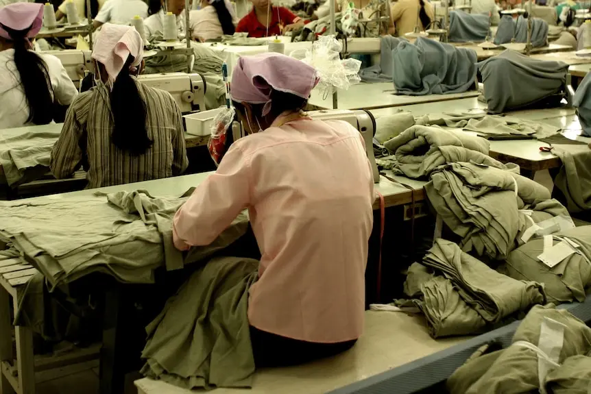 The backs of four women bent over sewing machines, making clothing.