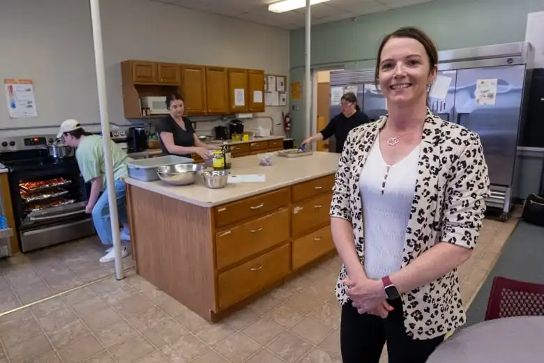 A person wearing a leopard-print cardigan stands in a kitchen, smiling.