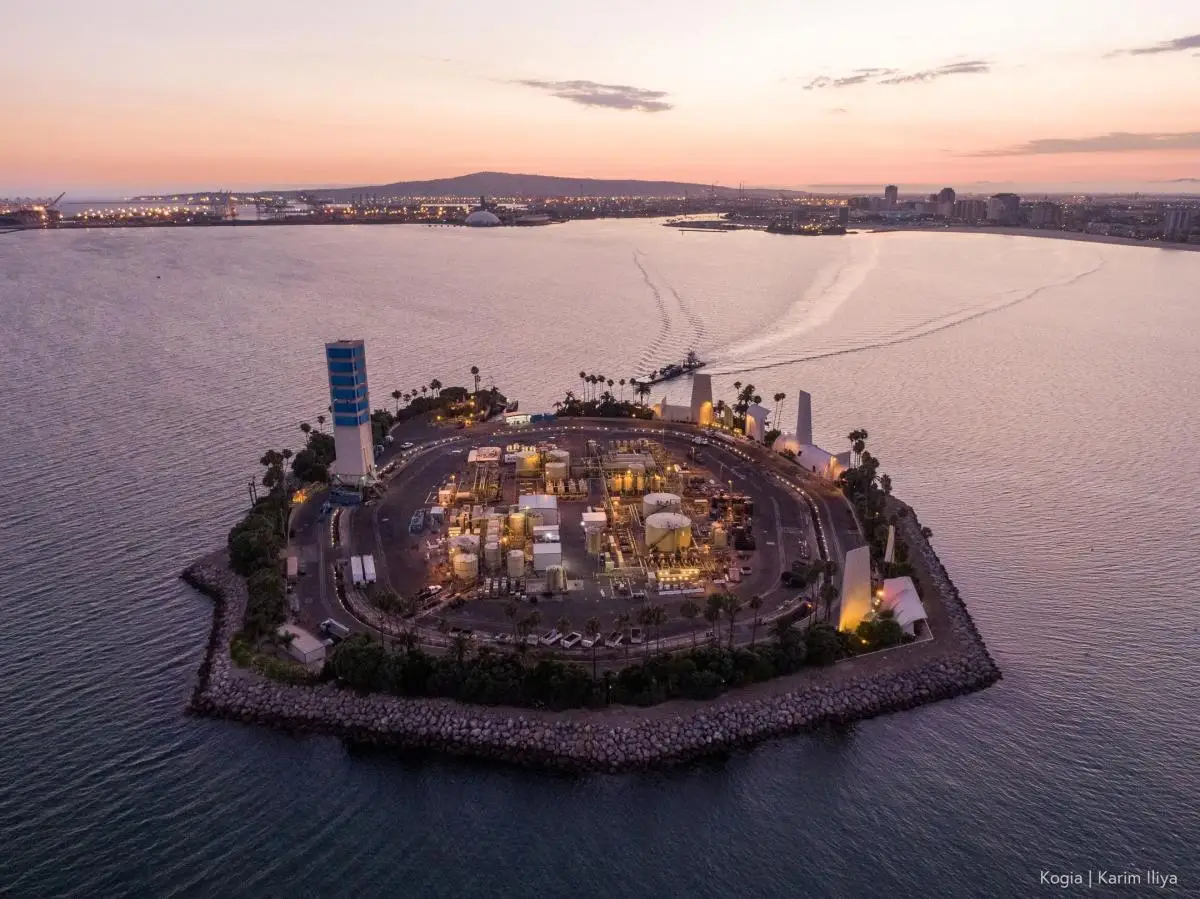 An aerial view of a man-made island with fossil-fuel infrastructure, at sunset