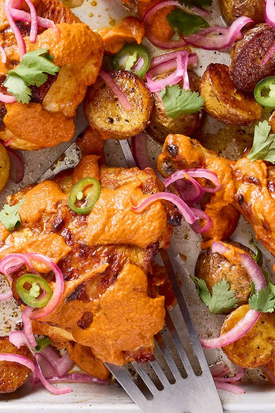 chicken thighs covered in a tikka masala sauce with pickled red onions and jalapenos on a sheet pan