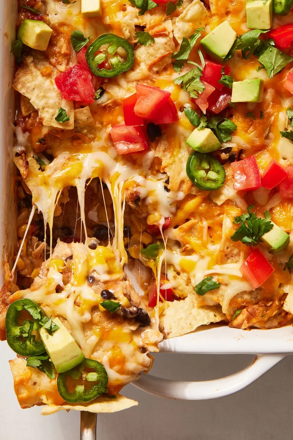 mexican chicken casserole topped with diced tomatoes, jalapenos and avocado