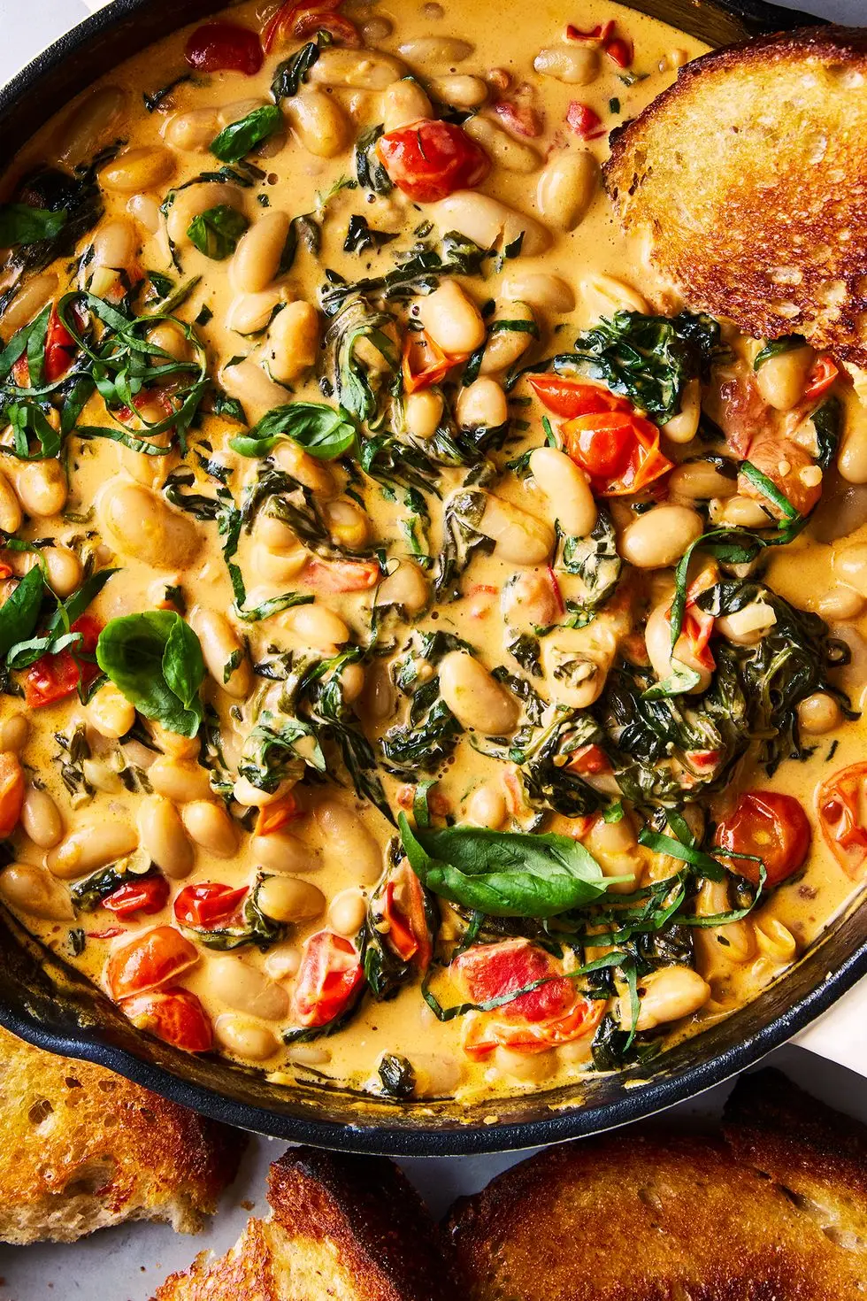 cast iron skillet filled with creamy tuscan white beans topped with basil, with toast alongside