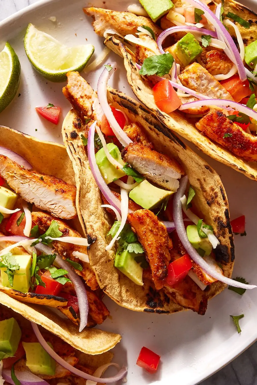 flour tortillas on a plate filled with chicken, tomatoes, avocado and red onion