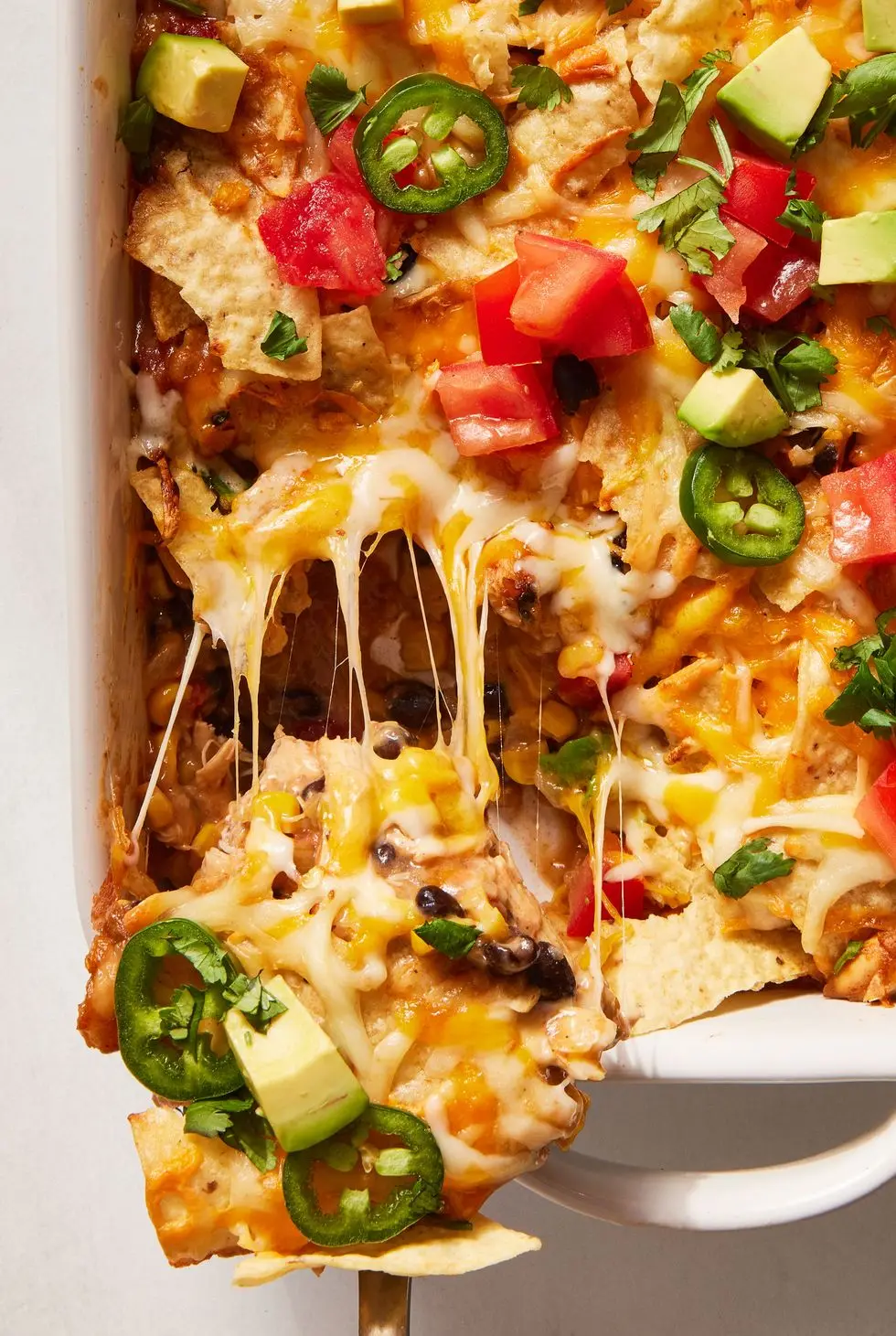 mexican chicken casserole topped with diced tomatoes, jalapenos and avocado