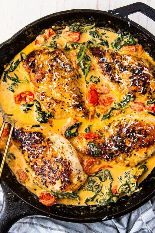 tuscan chicken in yellow cream sauce with spinach and tomatoes in a black cast iron skillet