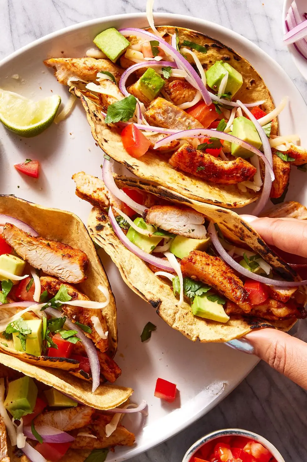 flour tortillas on a plate filled with chicken, tomatoes, avocado and red onion