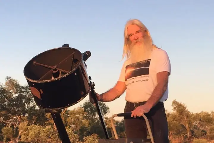 A man stands on a ladder beside a telescope