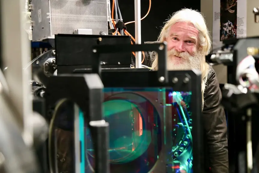 Bearded smiling man beside giant telescope