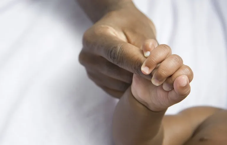 A baby's hand holding on to an adult's finger.