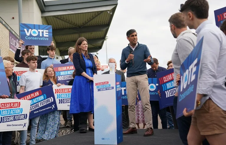 Surrounded by supporters with signs, Michelle Donelan, Secretary of State for Science, Innovation and Technology listens as Prime Minister Rishi Sunak speaks during a visit to Melksham Town Football Club.